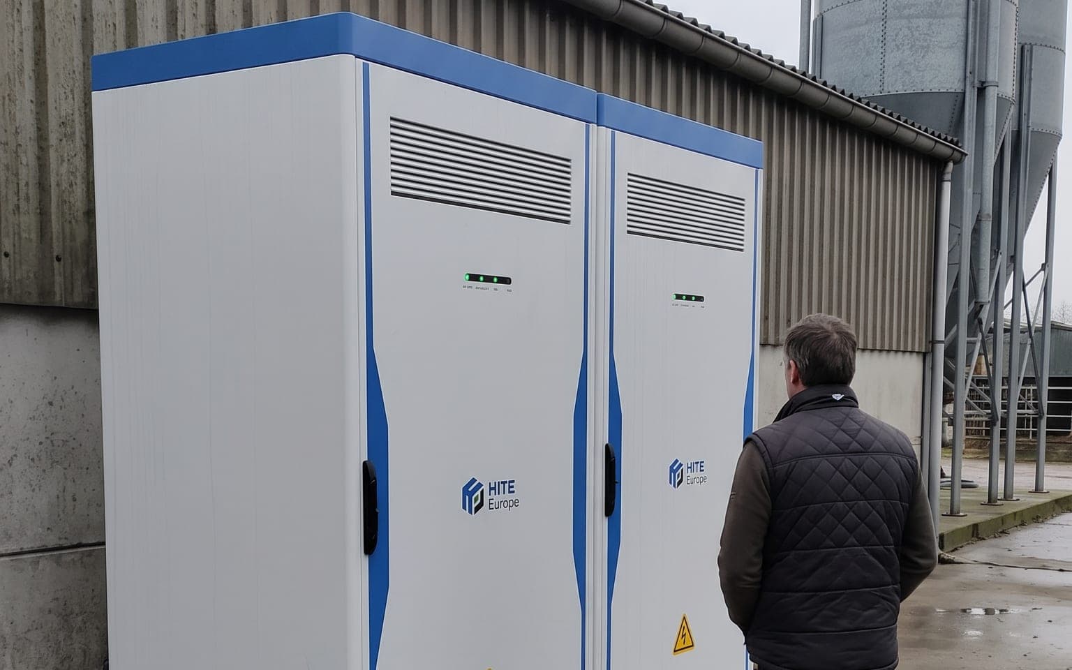 Twee batterijkasten tegen een loods op een landbouwbedrijf, met een voedersilo ernaast